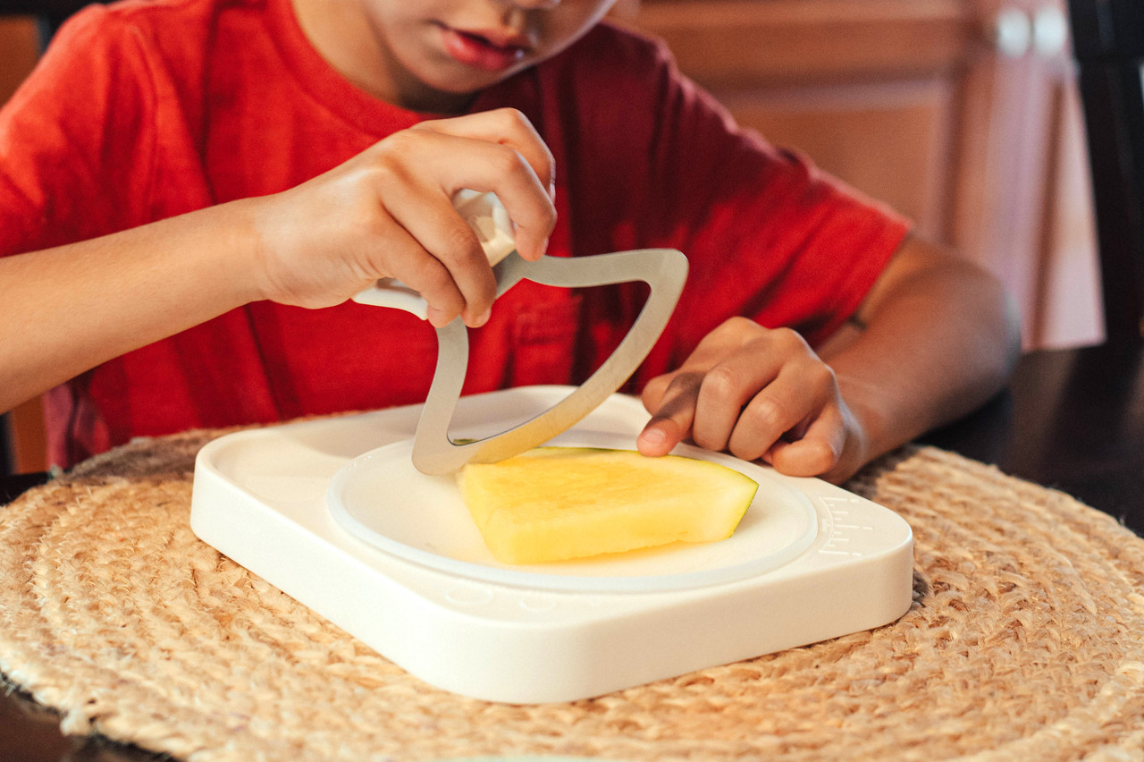 A child using the Holstead safety knife to slice watermelon on the cutting board